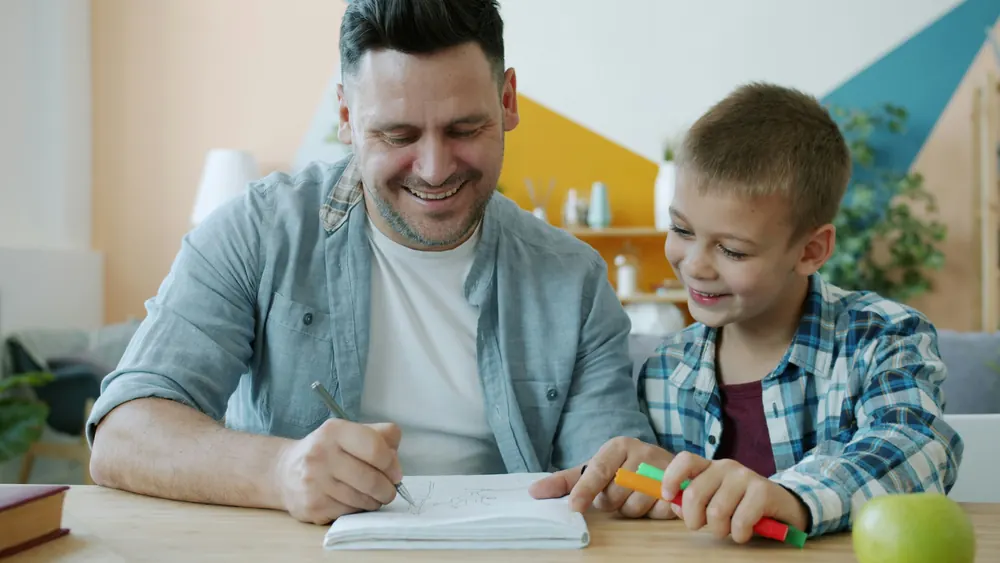 A father and son smiling as they work through homework together